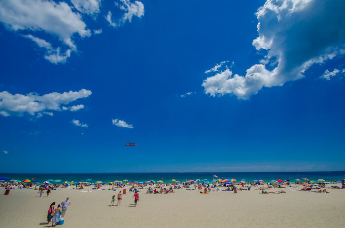 Beach scene with colorful umbrellas and people enjoying the sun, showcasing amazing views of the ocean under a clear blue sky.
