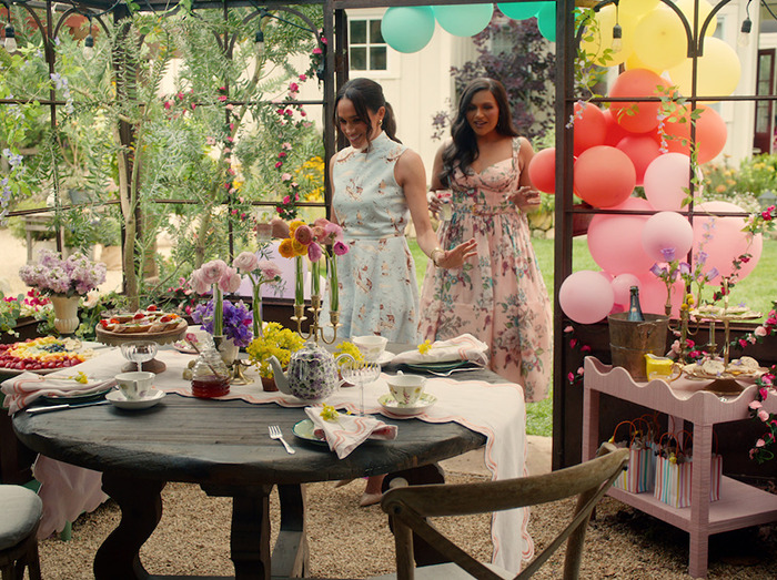 Meghan Markle with guest in floral dresses entering a garden party setting with a decorated table, emphasizing lifestyle series ambiance.