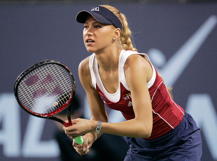 Tennis star Anna Kournikova poised with a racket on the court, wearing athletic gear and a visor.