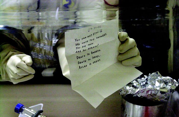 Gloved hands holding an anthrax threat letter in a lab, related to overlooked historical events.