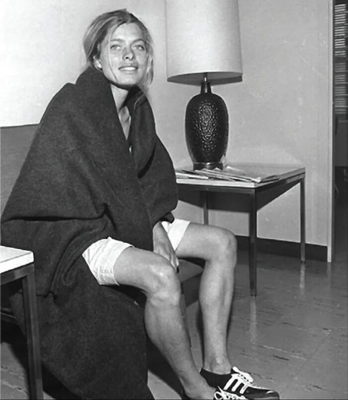 A person casually sitting with a blanket, legs crossed, historical cool vibe, beside a table lamp.