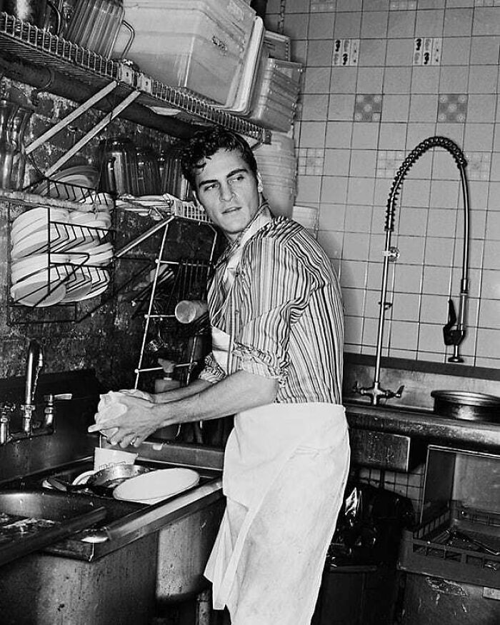 Young man washing dishes in a retro kitchen, black and white photo, showcasing history cool kids theme.