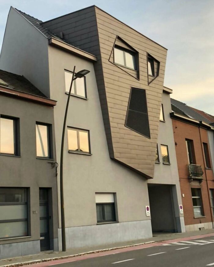 Oddly designed house with slanted shapes and windows, appearing like a face, in a neighborhood setting.