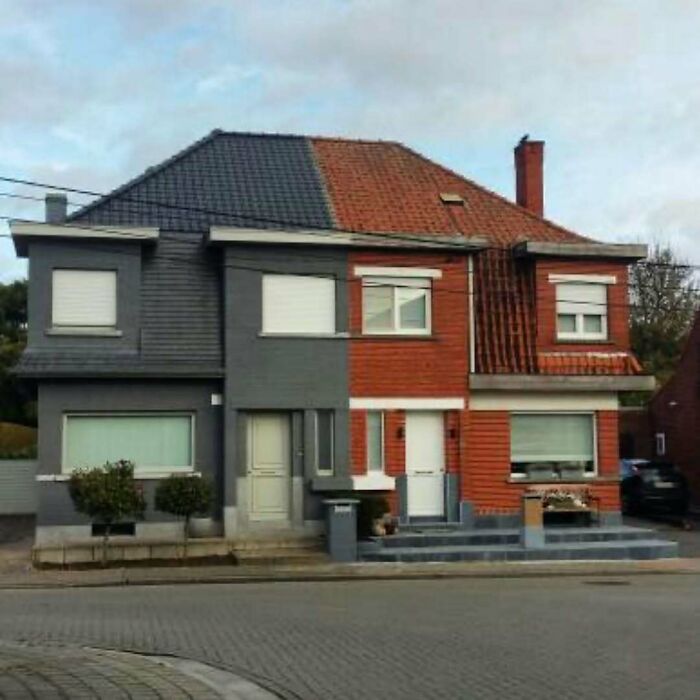 Oddly designed house with contrasting colors, featuring a gray and red split facade and mismatched roof tiles.