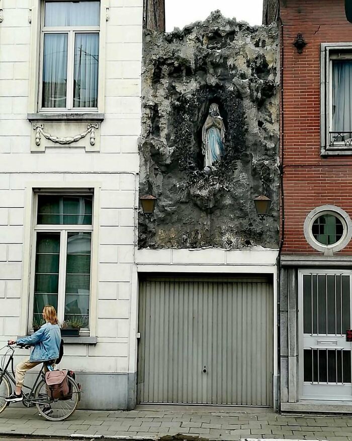 Bad house design with a rocky facade featuring a Virgin Mary statue, beside a cyclist on the street.