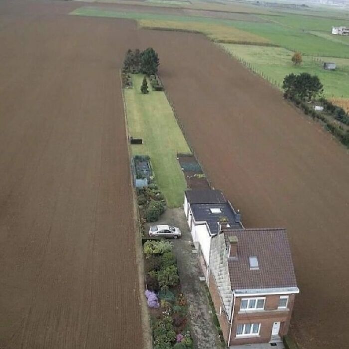 A hilariously bad house with a narrow garden strip stretching into a field, spotted by a Belgian individual.