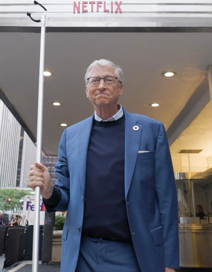 Man in a blue suit holding a pole, standing under a Netflix sign outdoors.