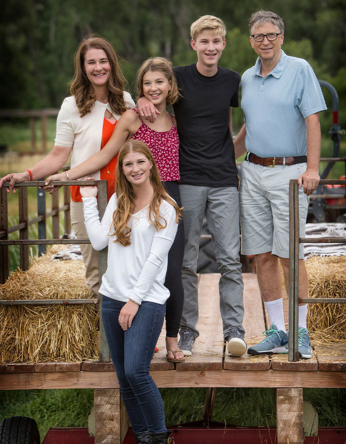 Group of five people on a wooden trailer with hay bales, outdoors.