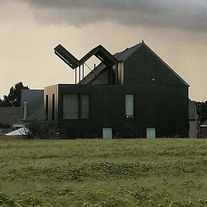 Unconventional house design with mismatched roof angles under a cloudy sky.