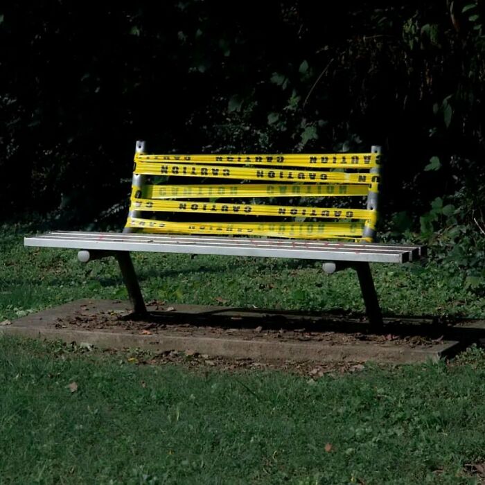 Garden bench wrapped in caution tape, creating a unique look in a grassy area.