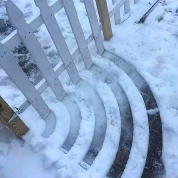 Unique garden steps in snow, showcasing creative curved design beside a white picket fence.