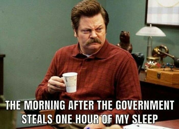 A man in an office holding a coffee cup with a tired expression, a humorous meme about losing sleep to daylight saving time.