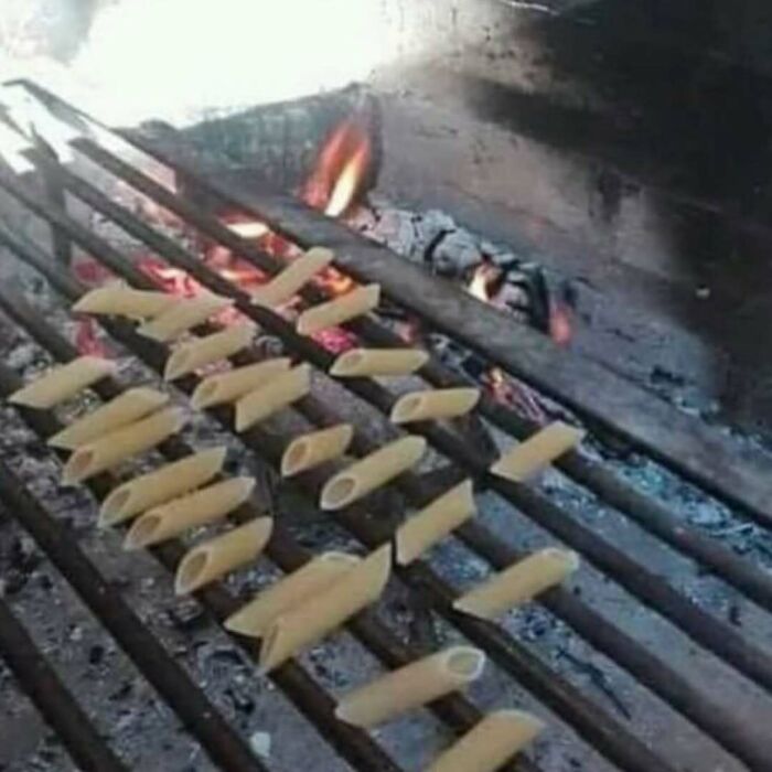 Confusing photo of uncooked penne pasta placed on a grill over open flames.