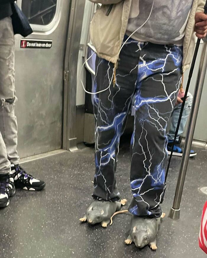 NYC local in lightning-patterned pants and rat-shaped slippers on the subway, showcasing bold New York fashion.