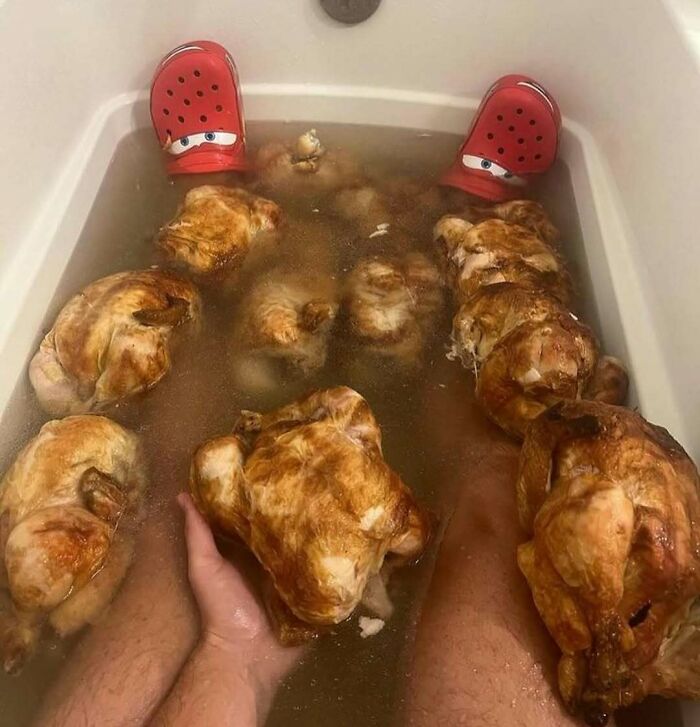 Person in a bathtub filled with roasted chickens, wearing red crocs, creating a confusing and funny scene without context.