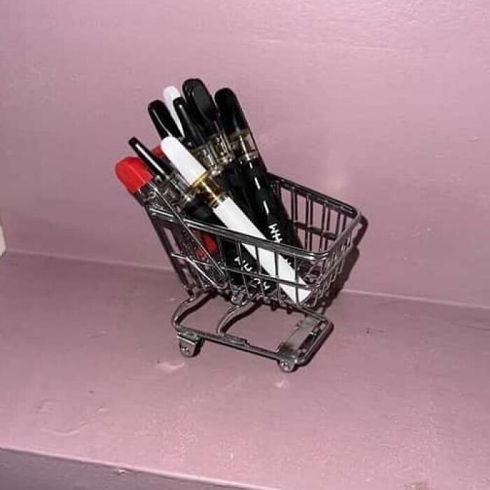 Mini shopping cart filled with pens, against a pink background; a confusing and funny photo.