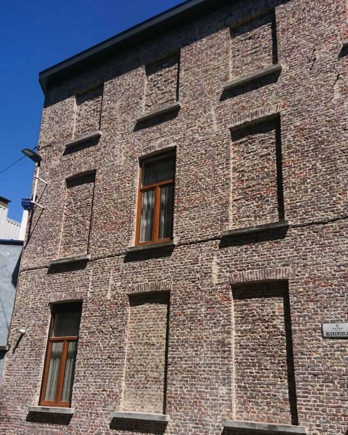 Brick building with mismatched windows and bricked-up sections, highlighting hilariously bad architecture choices.