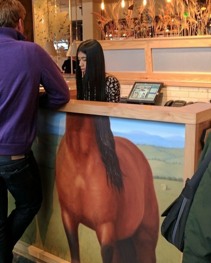 Bizarre photo of a woman behind a counter painted with a horse body, creating an optical illusion.