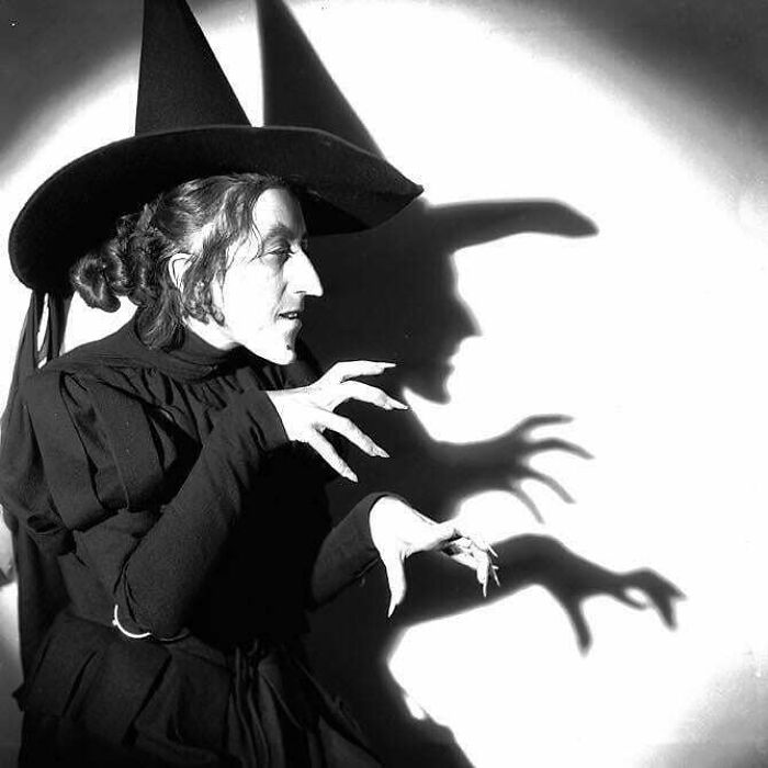 A person dressed as a witch in classic black costume casting a shadow on the wall, evoking vintage Halloween charm.