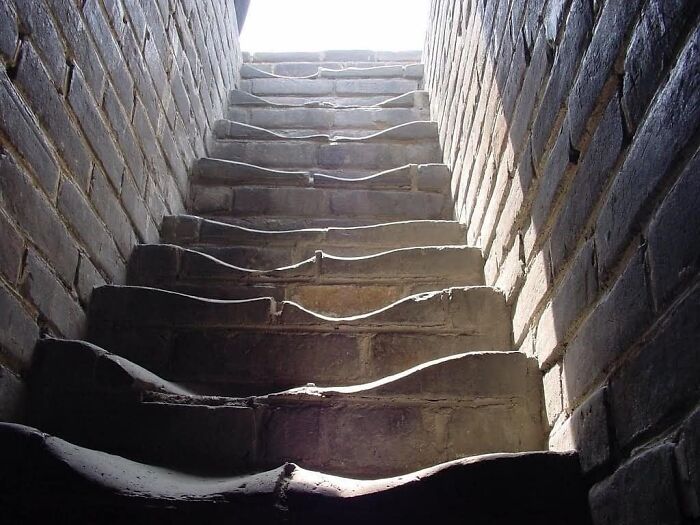 Stone steps leading upwards between brick walls, illuminated by sunlight.
