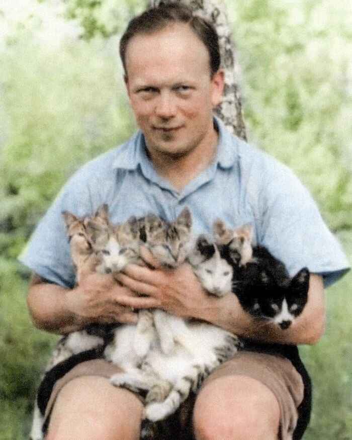 Man smiling, sitting with six kittens in his arms, outdoors.