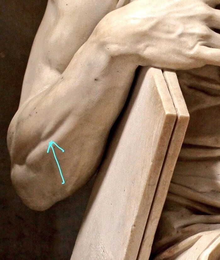 "Close-up of a marble sculpture's arm with a blue arrow, highlighting historical art details."