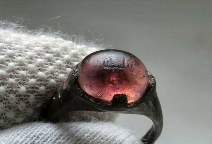 Ancient ring with a purple gemstone, held by a gloved hand, showcasing a historical artifact from the past.
