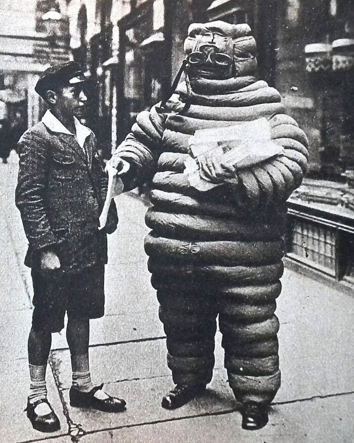 Young boy conversing with a person in a vintage bulky suit on a city street, capturing a moment from the past.