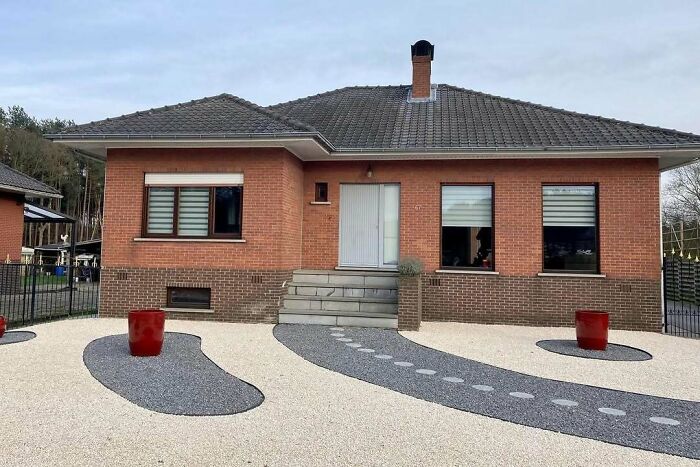 Brick house with mismatched landscaping, featuring oversized pots and surreal pathways, reflecting hilariously bad house design.