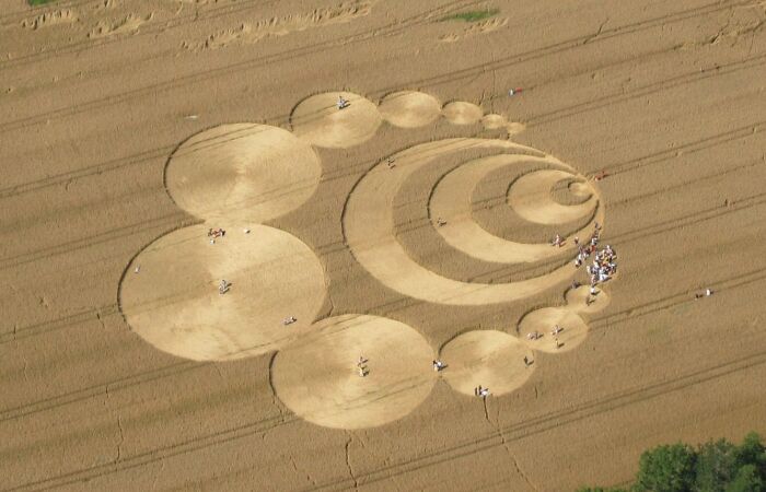 Crop circles in a field, a classic example of weird unsolved mysteries, with people inspecting the pattern.