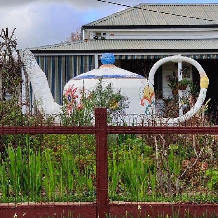Unique garden with a giant teapot sculpture surrounded by greenery, showcasing creative landscaping.