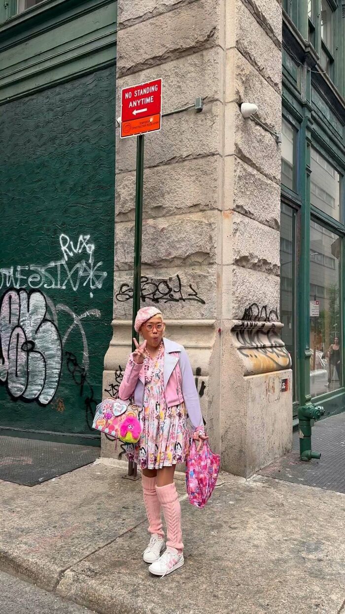 New York local in colorful outfit with pink accents, standing on a graffiti-tagged street corner.
