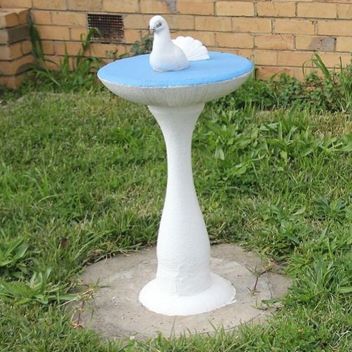 Unique garden decoration featuring a white bird sculpture on a pedestal in a grassy area.
