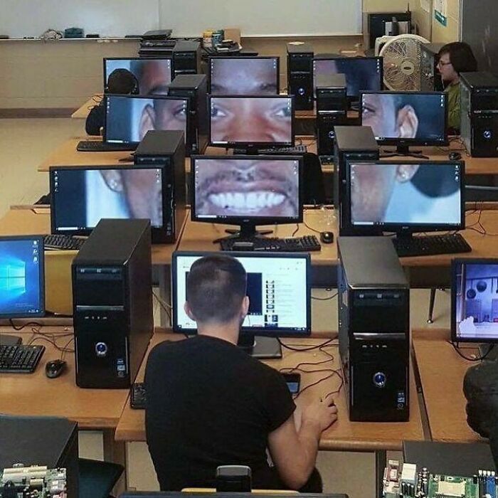 A room full of computers displaying a zoomed-in face, creating a confusing and funny scene without any context.