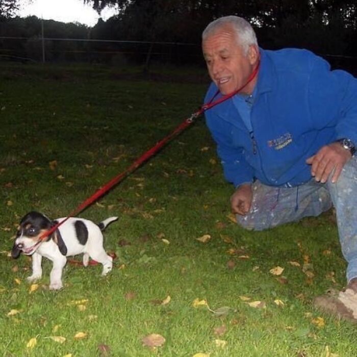 A man and a small dog on a leash, with the leash wrapped around his neck, in a funny and confusing outdoor scene.