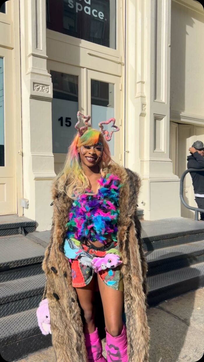 NYC local in vibrant, experimental fashion with colorful outfit and fur coat, standing outside on a sunny day.