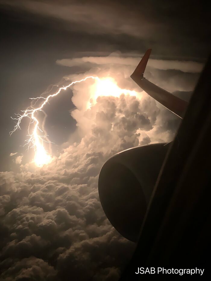 Airplane view of lightning storm above clouds, highlighting nature disaster resilience.