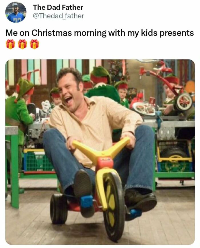 Dad joyfully riding kids' tricycle indoors, surrounded by Christmas decorations and elves.