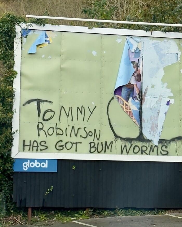 Graffiti on a billboard reads "Tommy Robinson has got b*m worms," showcasing British humor.