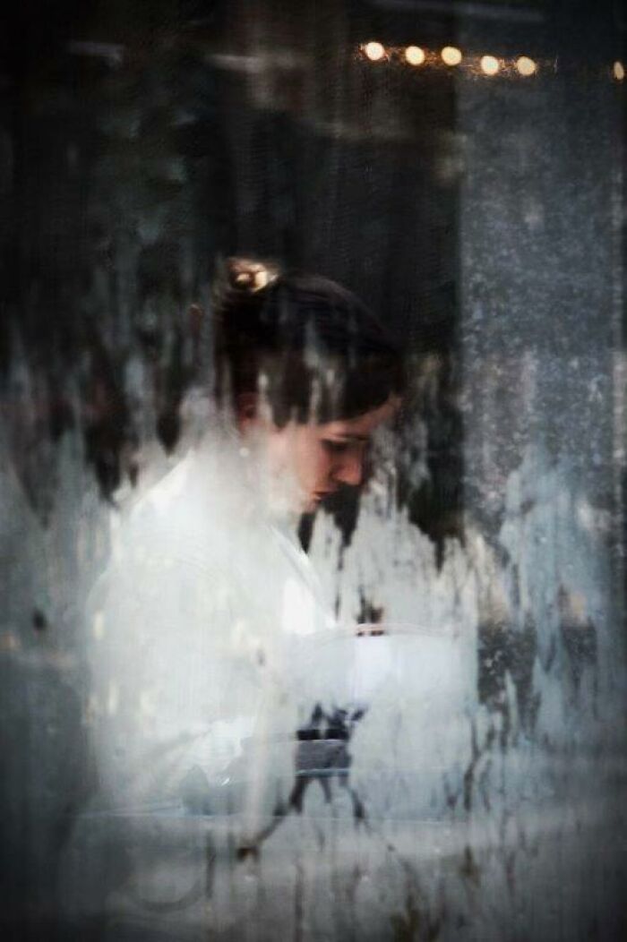 Woman seen through a textured window, capturing an everyday moment with Nadia Eeckhout’s artistic lens.