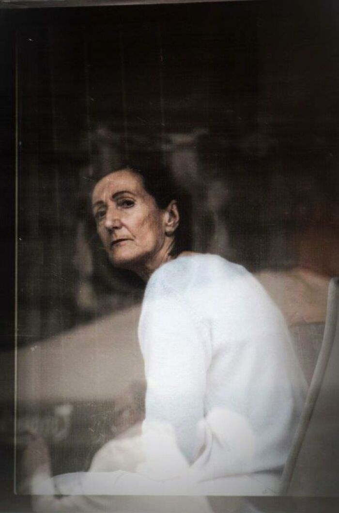 Woman in a white sweater gazing through a window, captured in an everyday moment through Nadia Eeckhout’s lens.