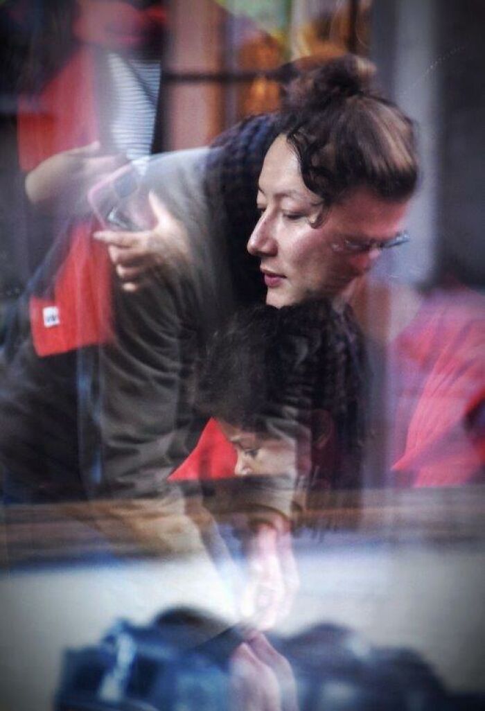 Nadia Eeckhout captures a candid moment of a woman with a child, reflecting through a glass window.