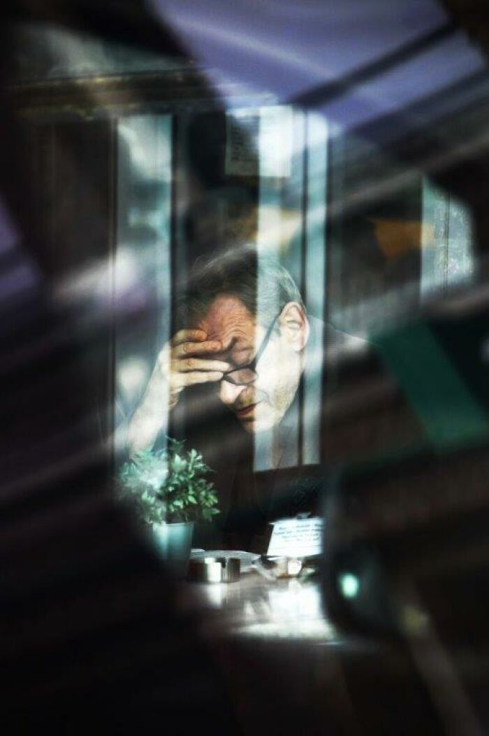 A man captured through a window with a hand on his forehead, embodying everyday moments by Nadia Eeckhout.