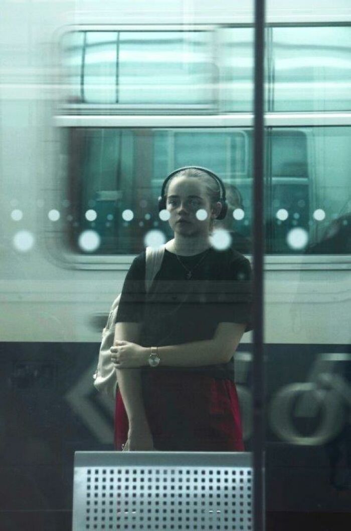 Person wearing headphones at a train station, captured through glass, embodying everyday moments.