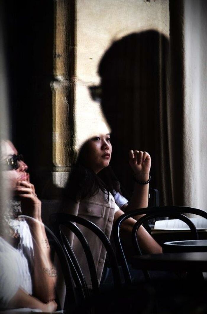 A thoughtful moment captured through Nadia Eeckhout’s lens, showing a woman sitting by a window with reflective light.