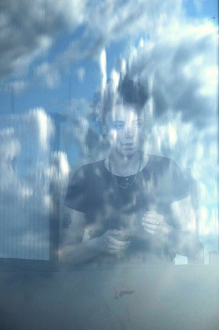 Person behind a glass with clouds, captured through Nadia Eeckhout's lens.