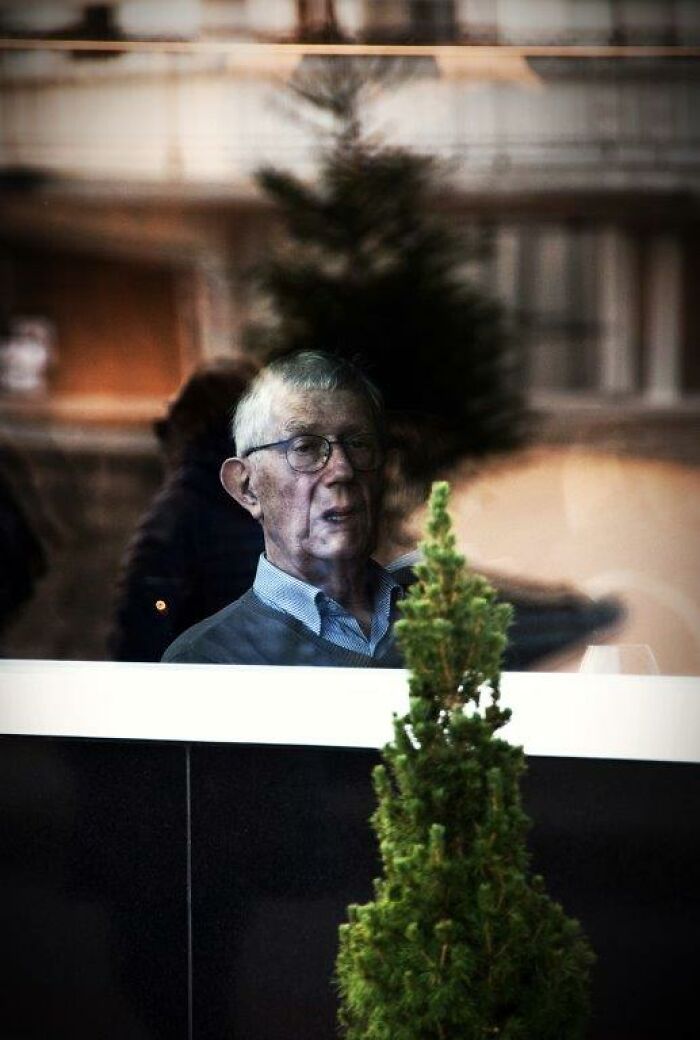 Elderly man seen through a window, captured in a candid moment by Nadia Eeckhout's lens.