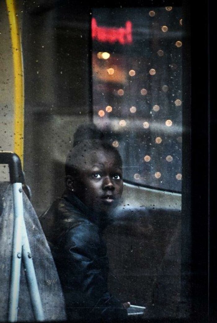 A person gazes through a bus window with bokeh lights outside, captured through Nadia Eeckhout's lens.