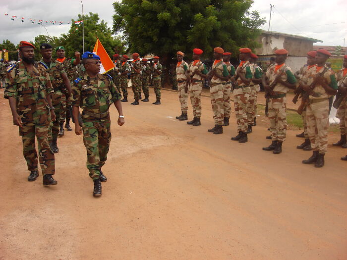 Military officers in uniform march during an overlooked historical event, with soldiers lined up on a street.