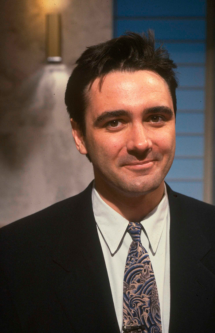 Tony Slattery in a suit and patterned tie smiling warmly.
